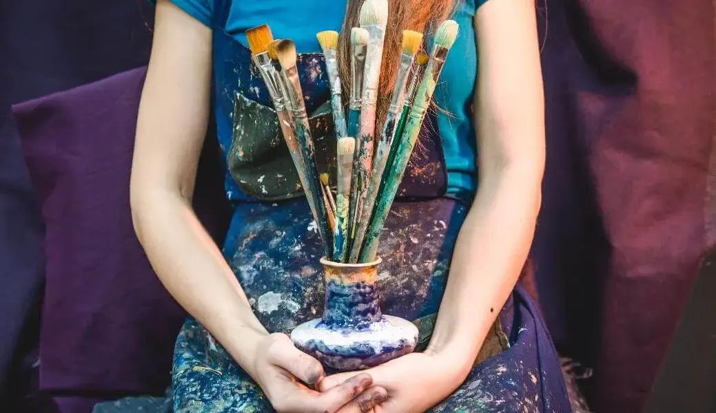 Artist covered in paint holding brushes